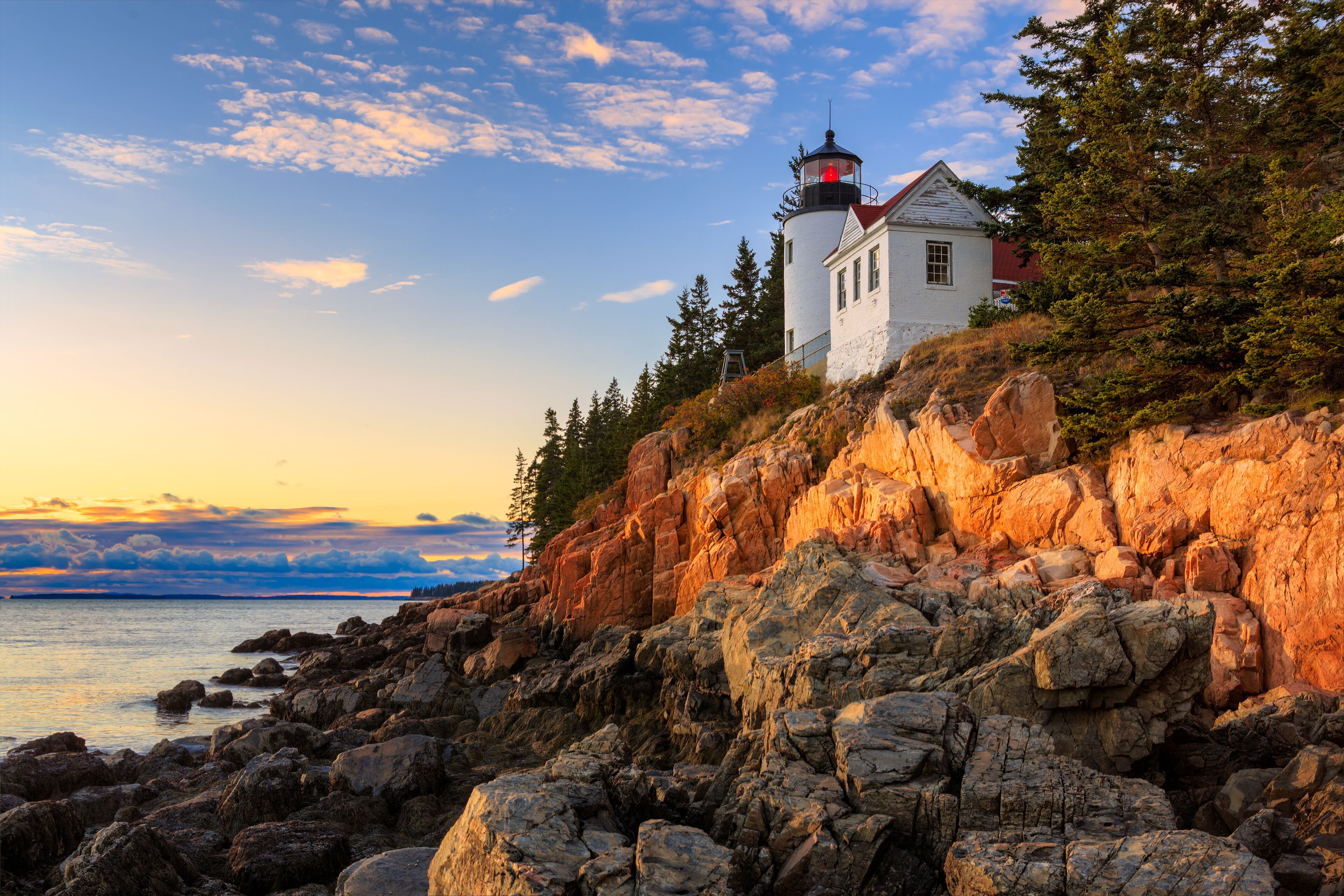 A lighthouse on a rocky cliff with a view of the ocean and a sunset sky.