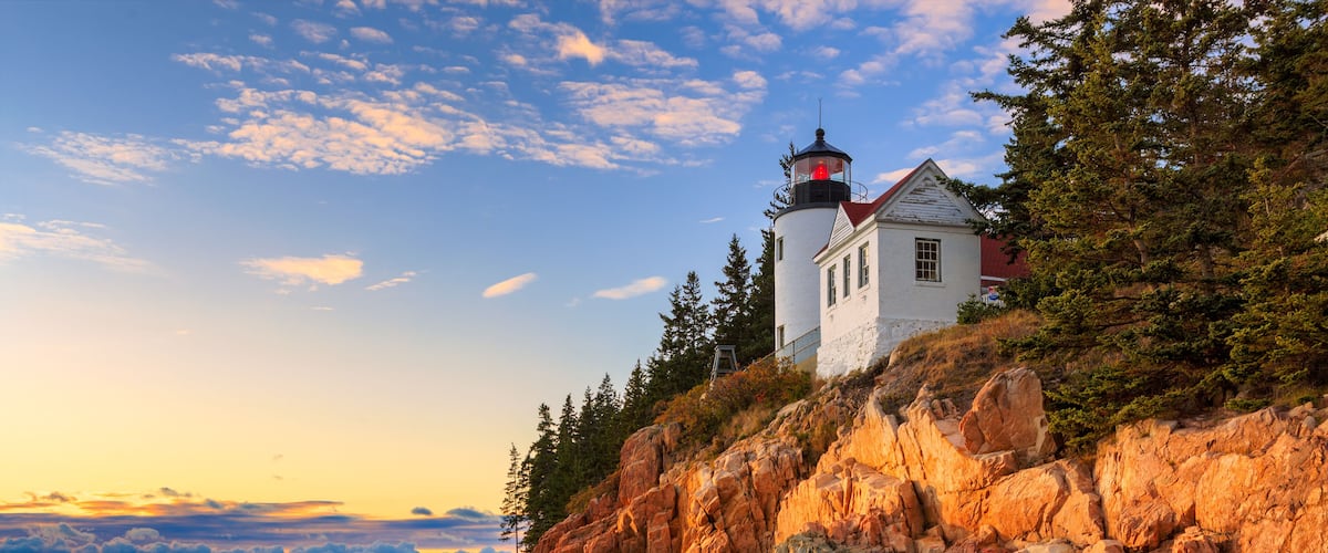 A lighthouse on a rocky cliff with a view of the ocean and a sunset sky.