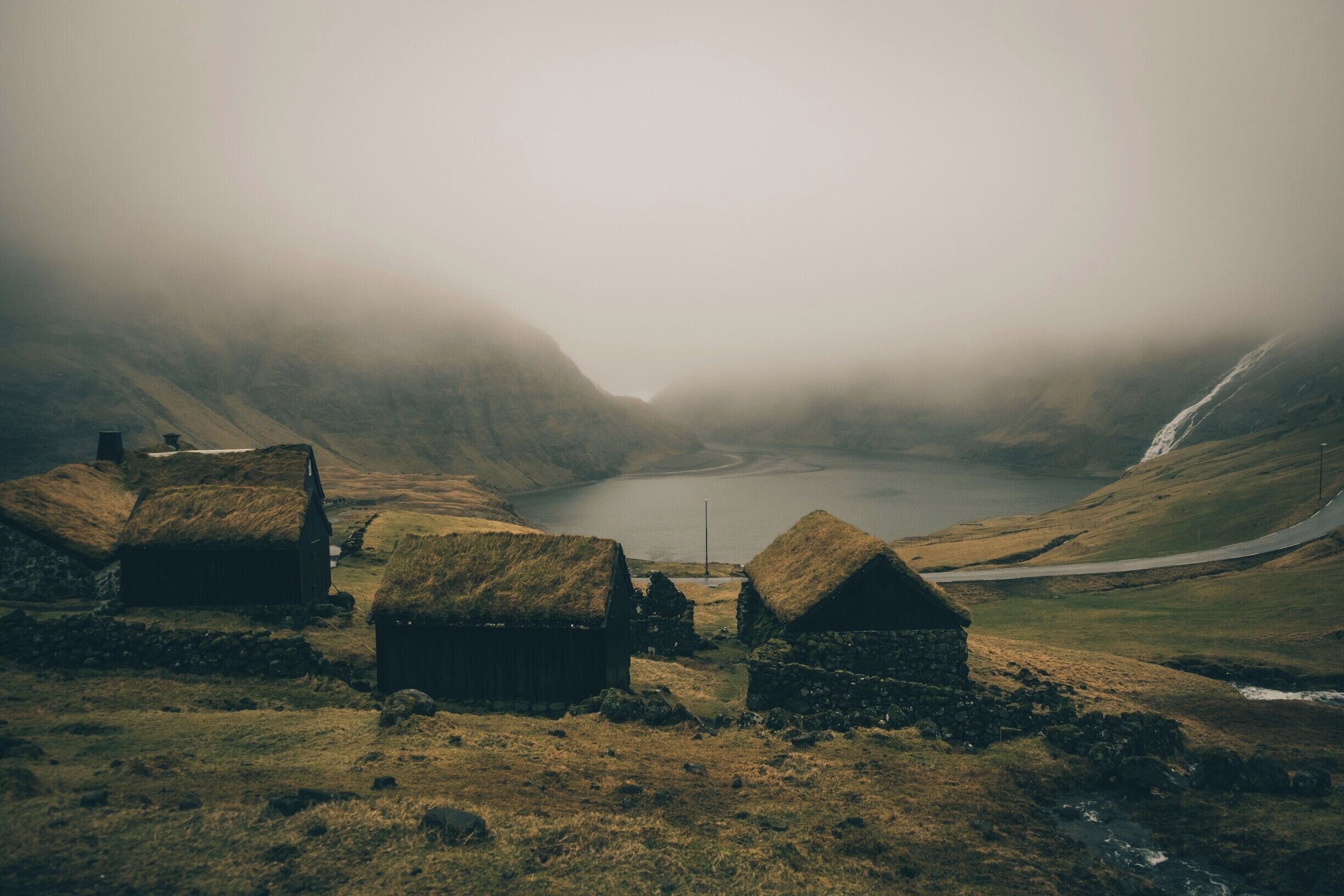 A misty landscape with thatched-roof houses, a lake, and a waterfall.