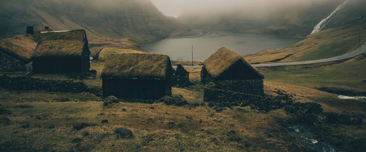 A misty landscape with thatched-roof houses, a lake, and a waterfall.