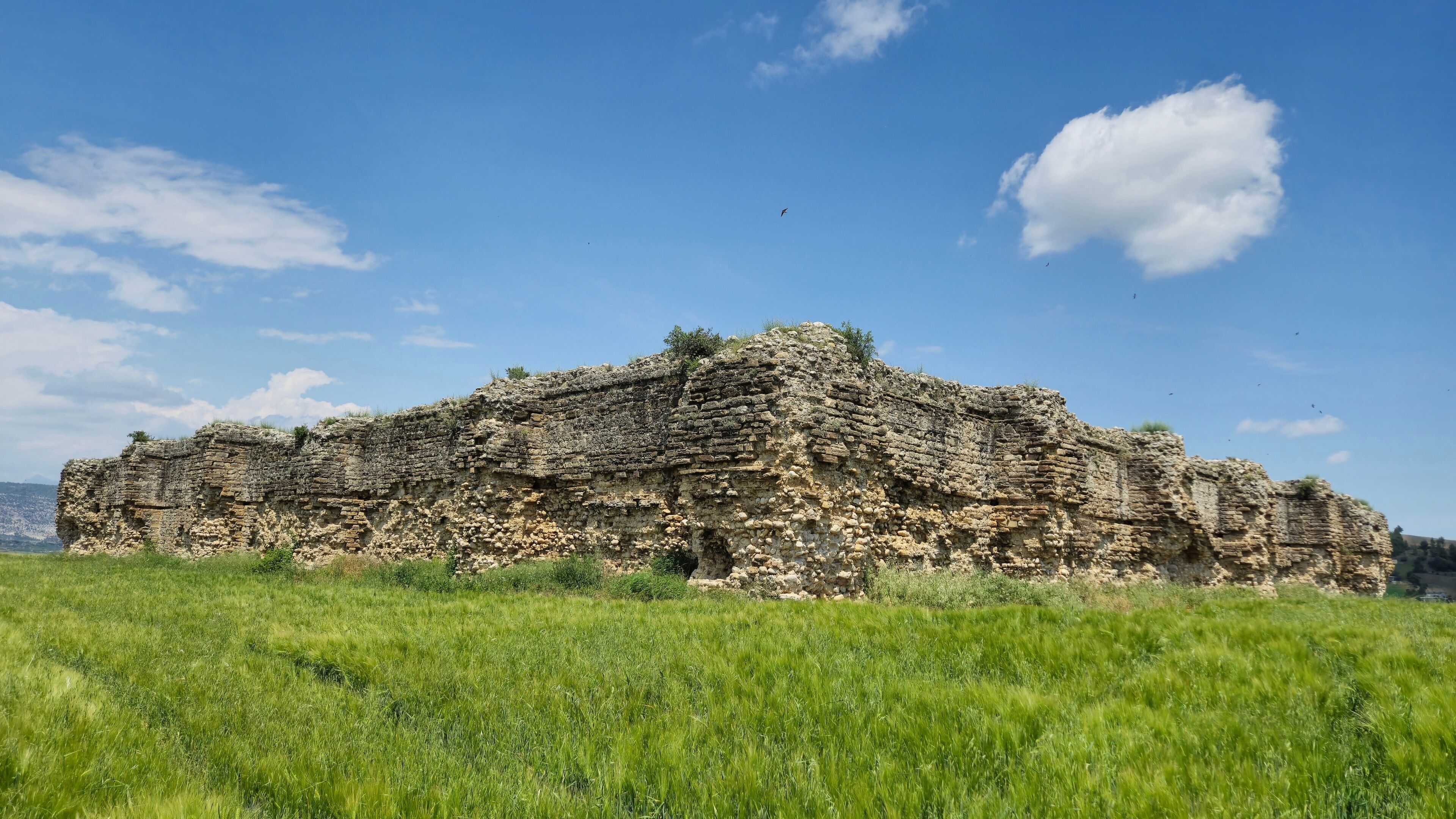 A large, ancient stone structure in a grassy field under a clear blue sky.