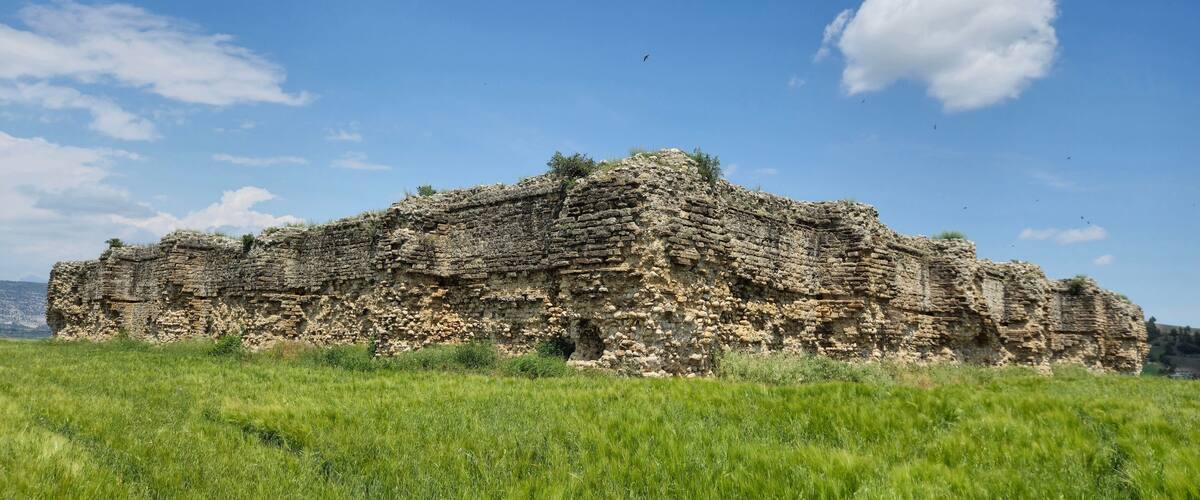 A large, ancient stone structure in a grassy field under a clear blue sky.