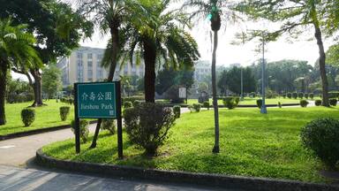 A sign for Jieshou Park surrounded by lush greenery and palm trees.