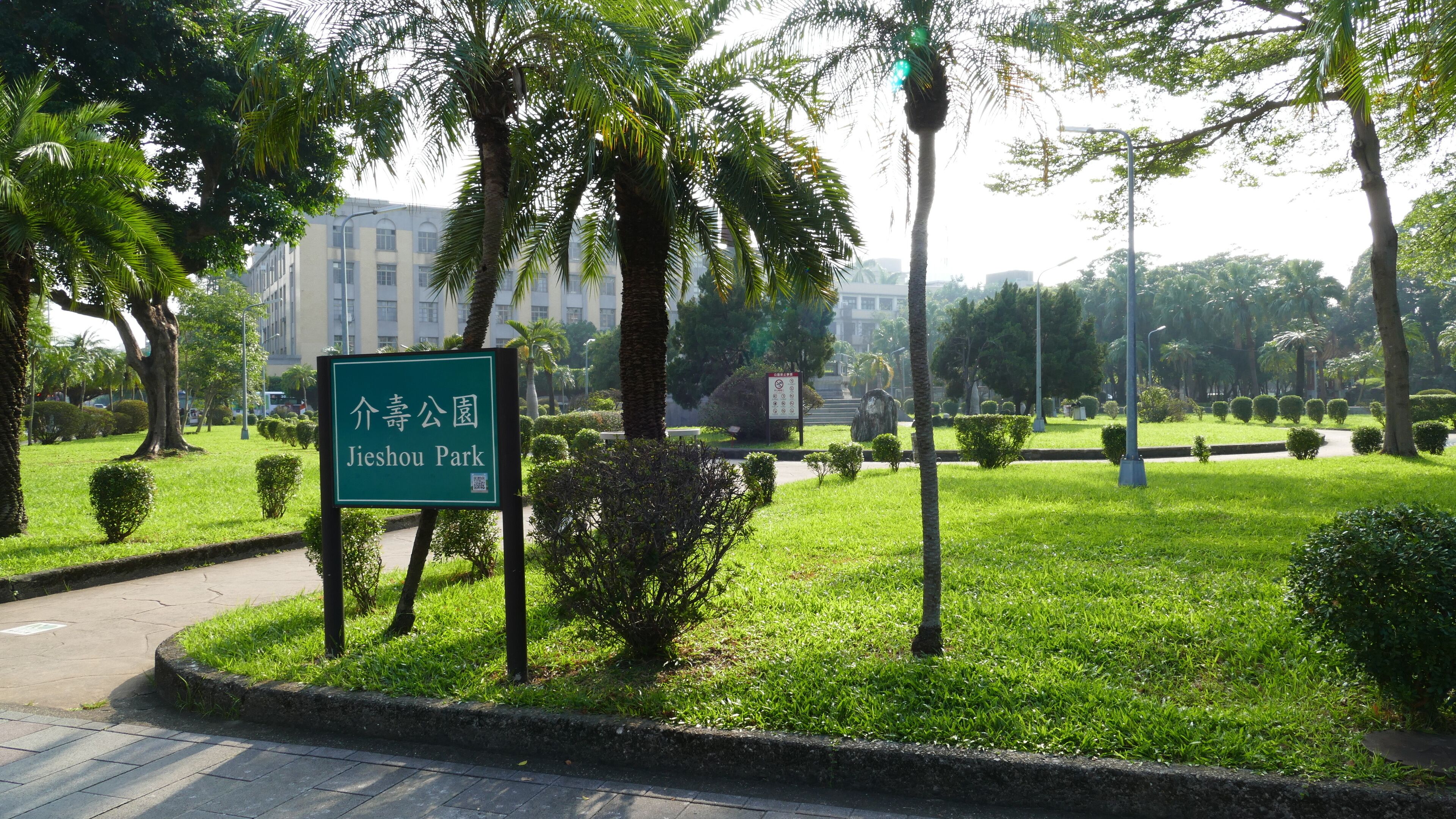 A sign for Jieshou Park surrounded by lush greenery and palm trees.