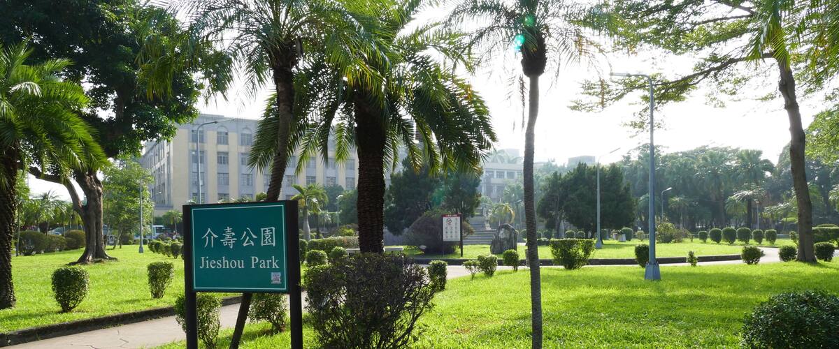 A sign for Jieshou Park surrounded by lush greenery and palm trees.