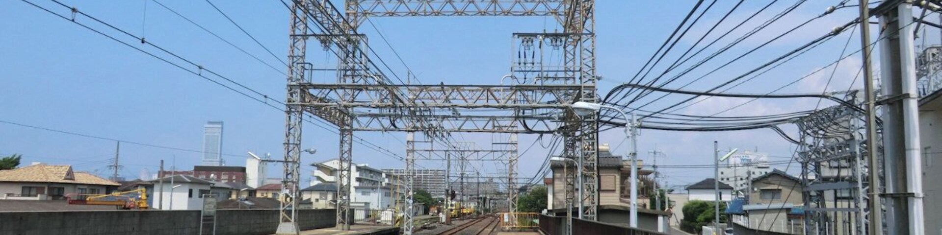 Un andén de tren con vías, líneas eléctricas elevadas y un cielo despejado.