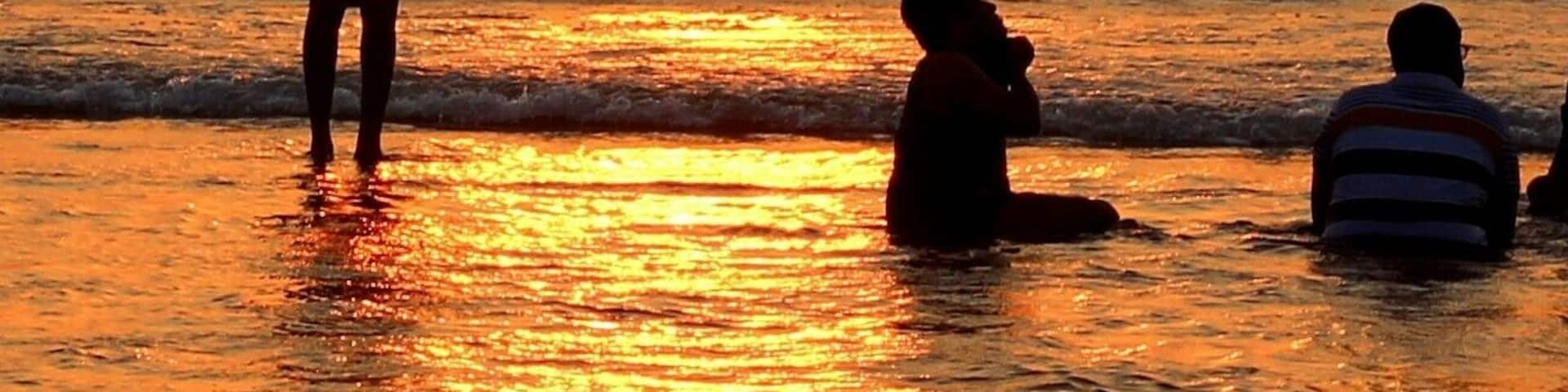 A sunset over the ocean with boats and people on the shore.