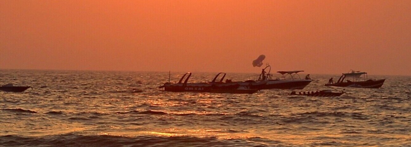 Una puesta de sol sobre el océano con barcos y gente en la orilla.