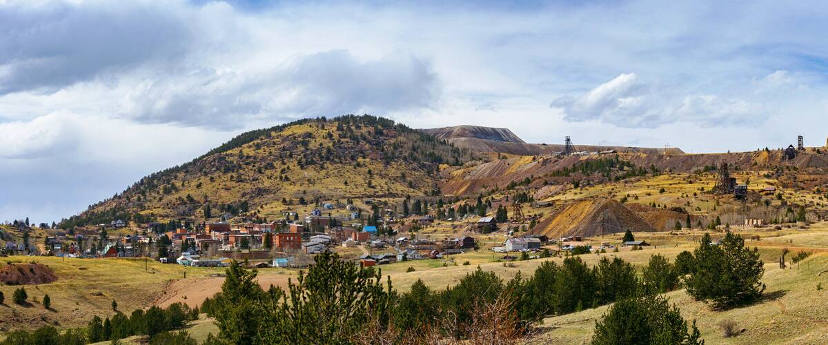 A wide view of Cripple Creek, Colorado, nestled against rolling hills and old mining structures. The historic town sits beneath a dynamic sky, its gold rush legacy still etched in the land.