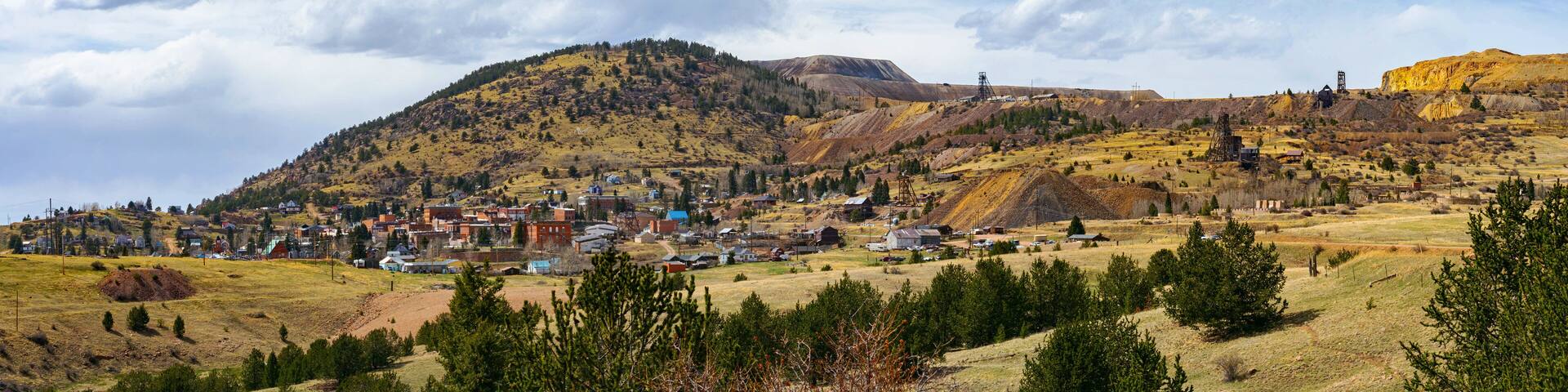 A wide view of Cripple Creek, Colorado, nestled against rolling hills and old mining structures. The historic town sits beneath a dynamic sky, its gold rush legacy still etched in the land.