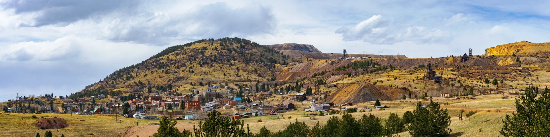 A wide view of Cripple Creek, Colorado, nestled against rolling hills and old mining structures. The historic town sits beneath a dynamic sky, its gold rush legacy still etched in the land.