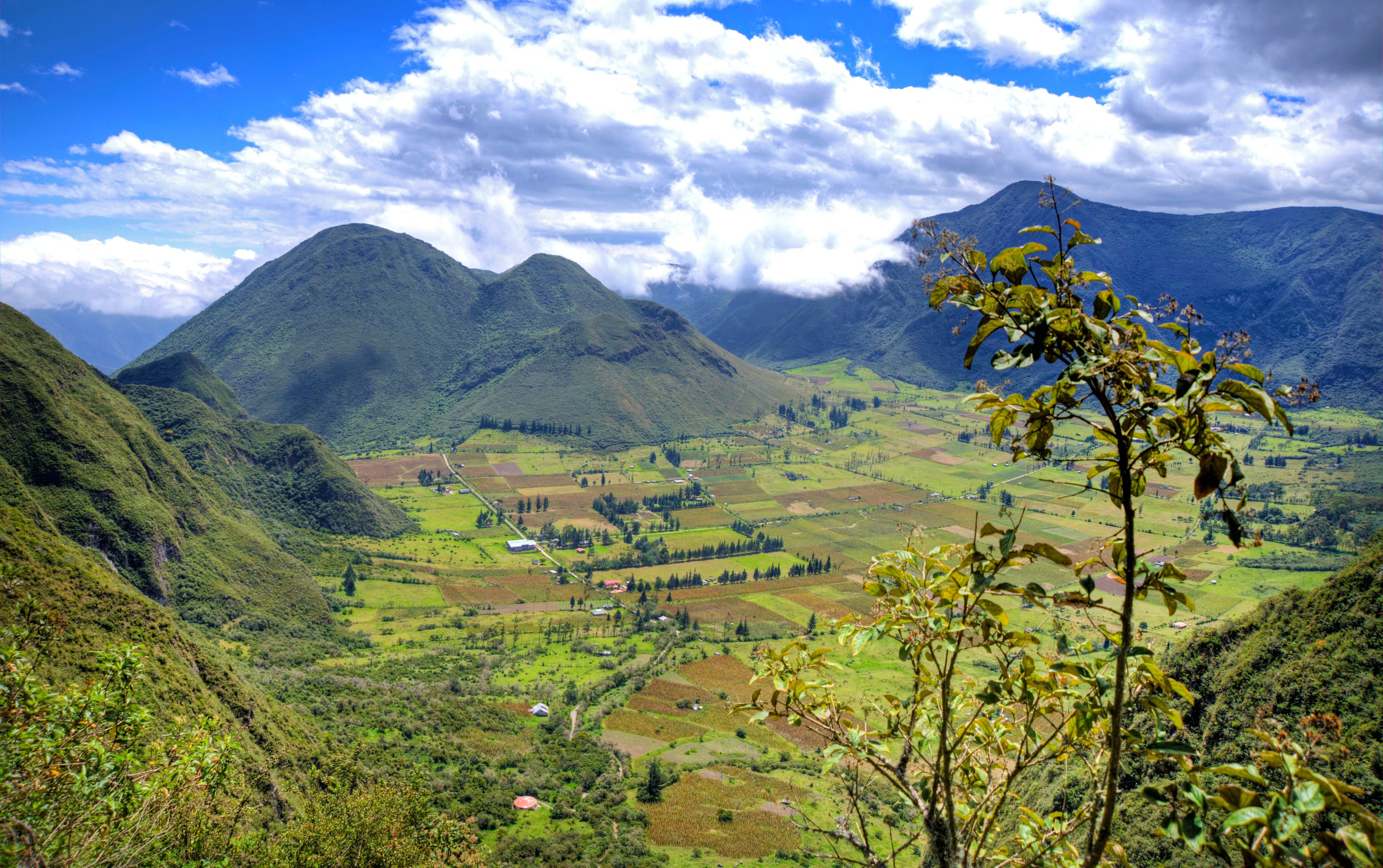 A mountainous landscape with lush green fields, a river, and a village.