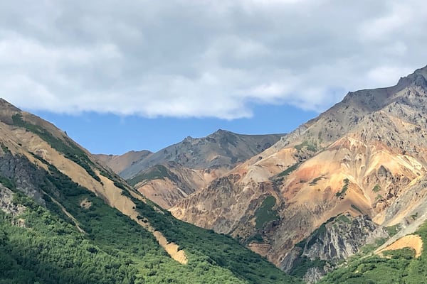 Un paysage montagneux avec des vallées verdoyantes et des pics rocheux, sous un ciel partiellement nuageux.