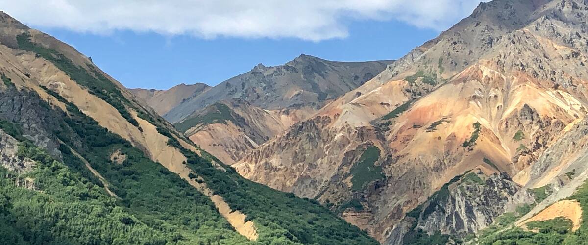 A mountainous landscape with green valleys and rocky peaks under a partly cloudy sky.