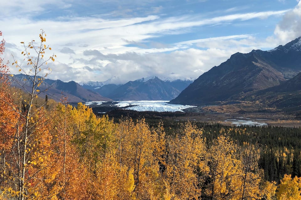 Een gletsjer in een bergachtig landschap met herfstkleurige bomen.