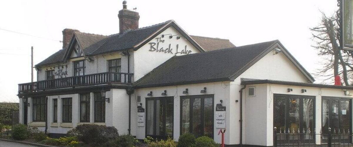 A white building with a black roof and balcony, named 'The Black Lake'.