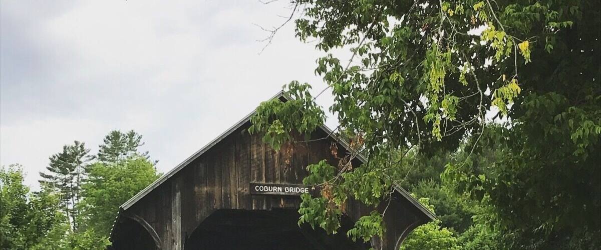 A wooden covered bridge labeled 'Coburn Bridge' in a lush, green forest setting.