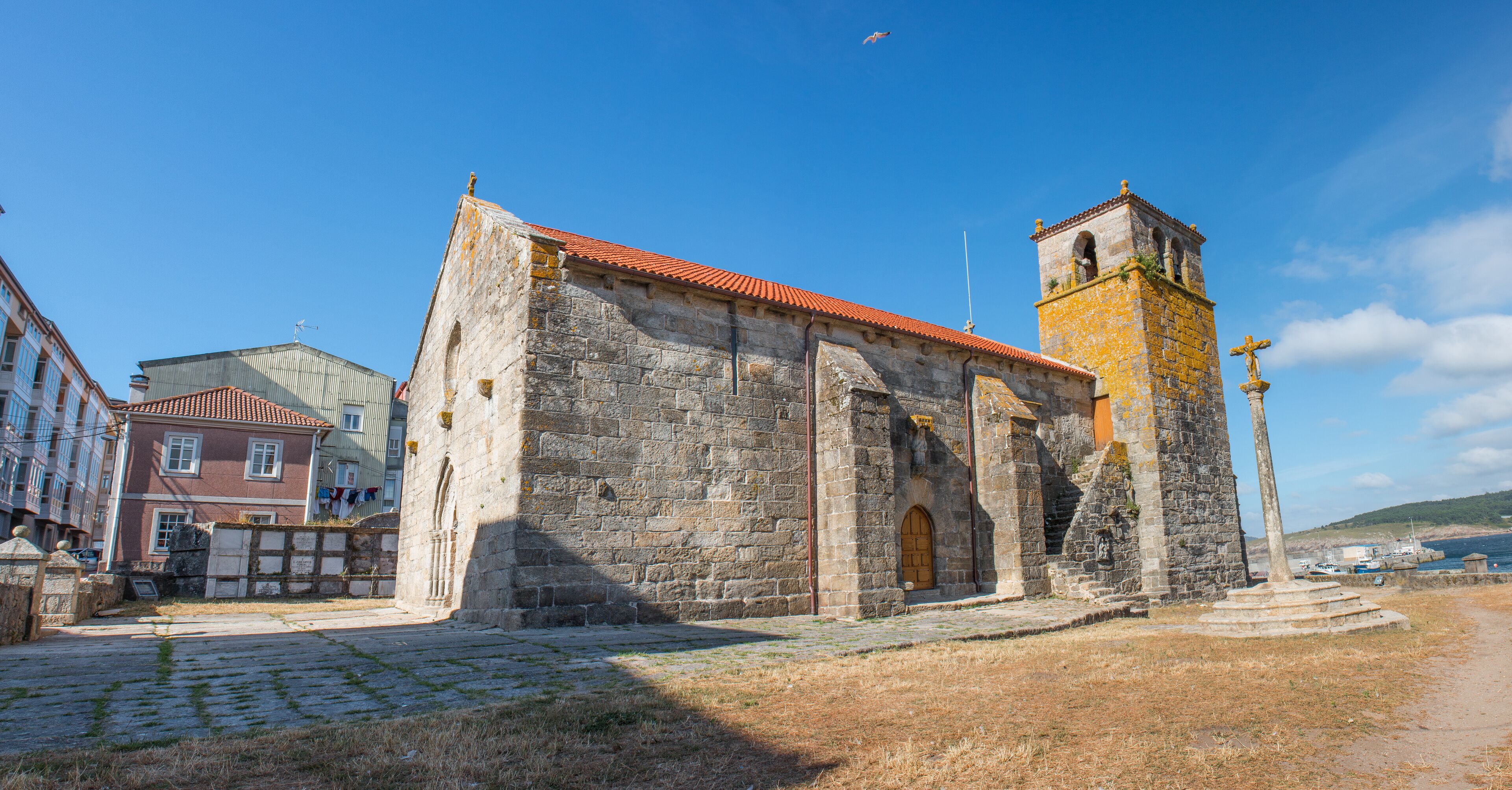 A historic stone church with a bell tower and a cross on top, surrounded by cobblestone streets and buildings.