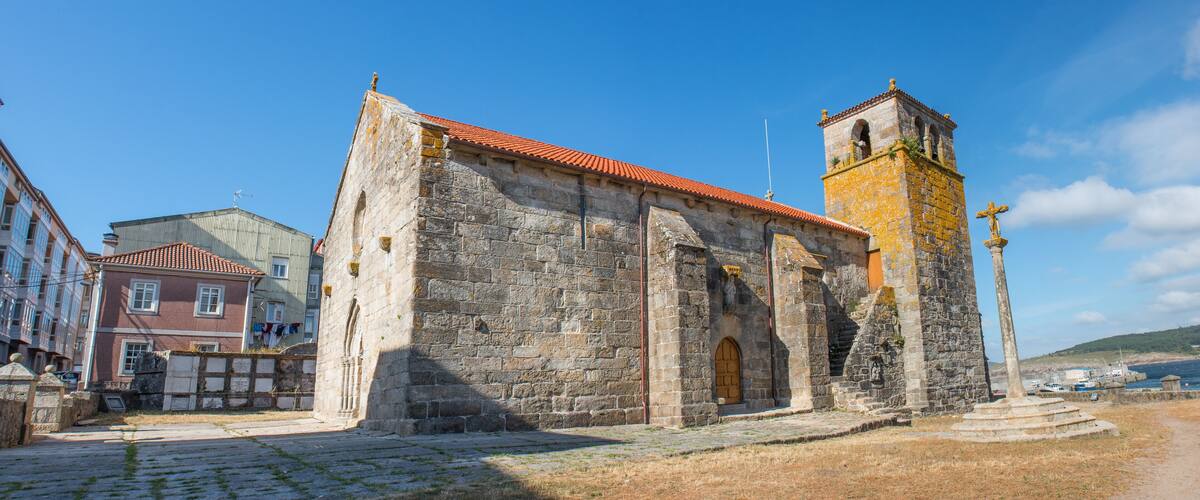 A historic stone church with a bell tower and a cross on top, surrounded by cobblestone streets and buildings.