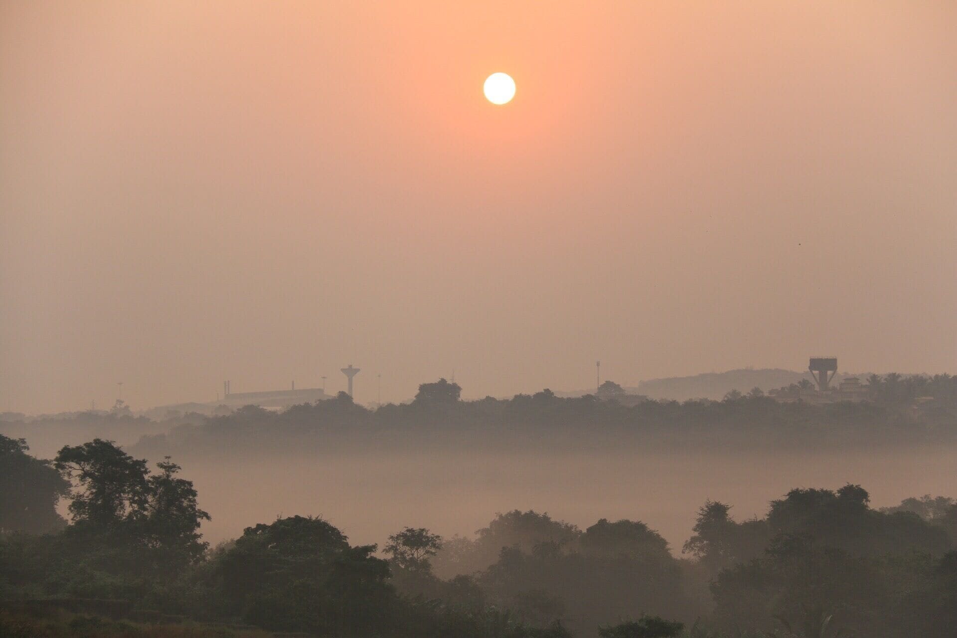 A hazy sunrise over a landscape with a prominent tower and trees.
