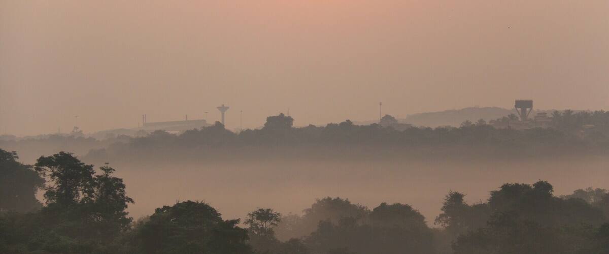 A hazy sunrise over a landscape with a prominent tower and trees.