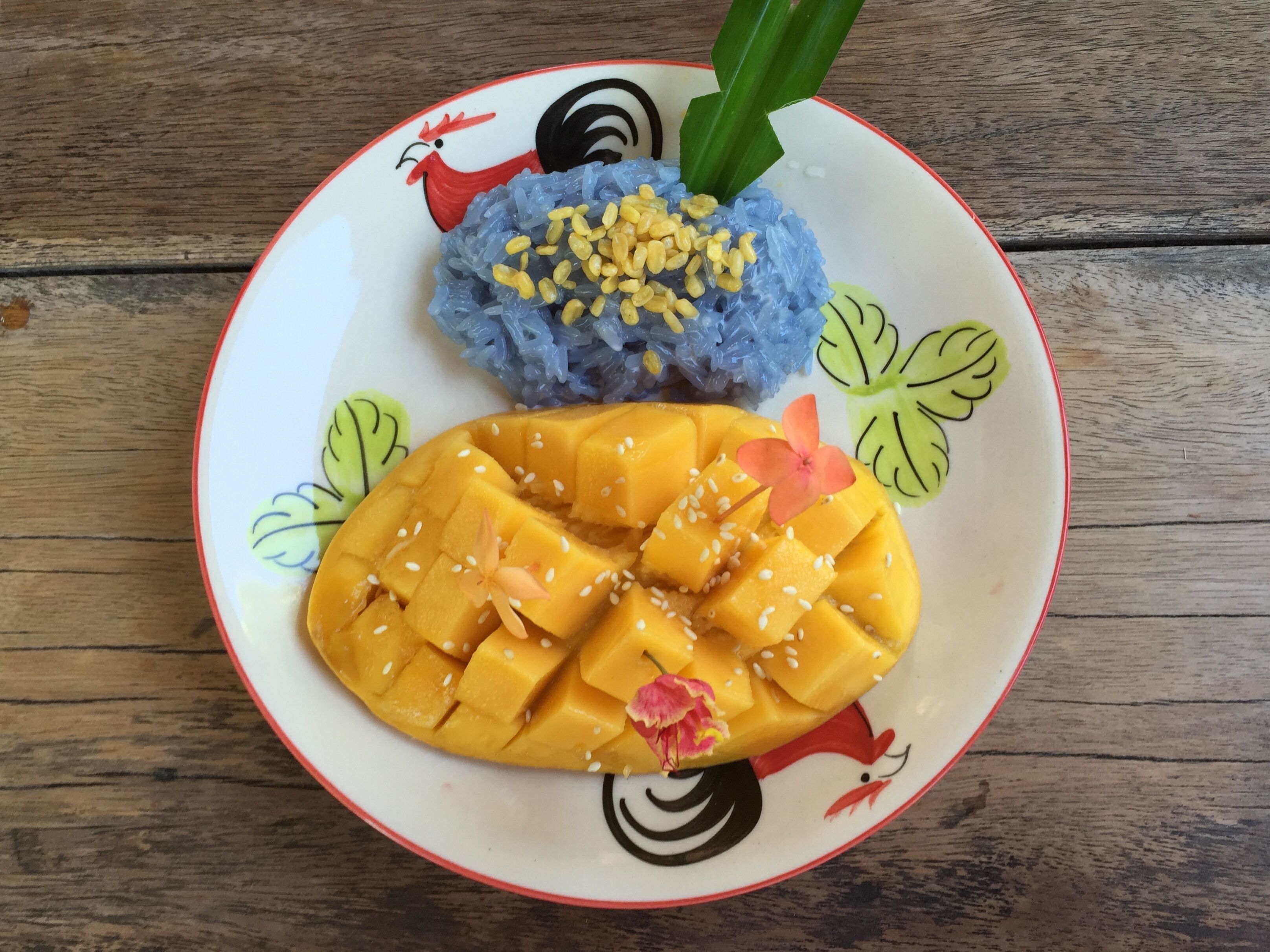 A plate with blue rice, mango slices, and a decorative leaf.