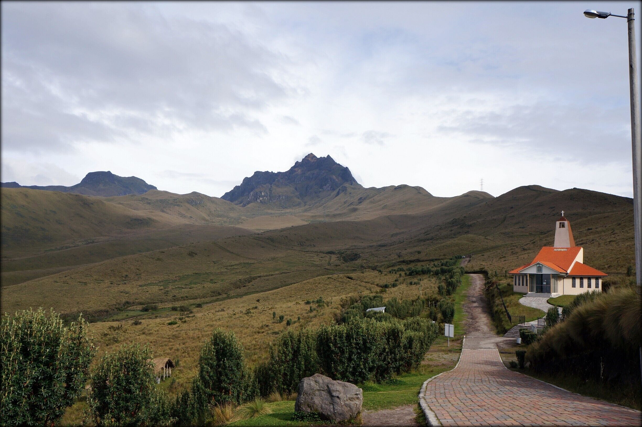 A rural landscape with rolling hills, a church with a red roof, and a mountain in the background.