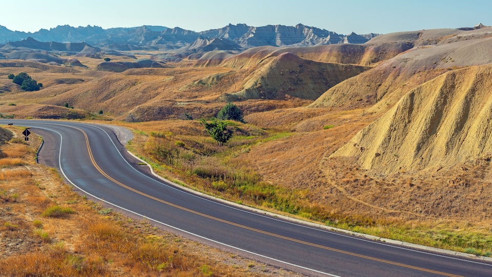 A winding road through a hilly landscape with sparse vegetation and distant mountains.