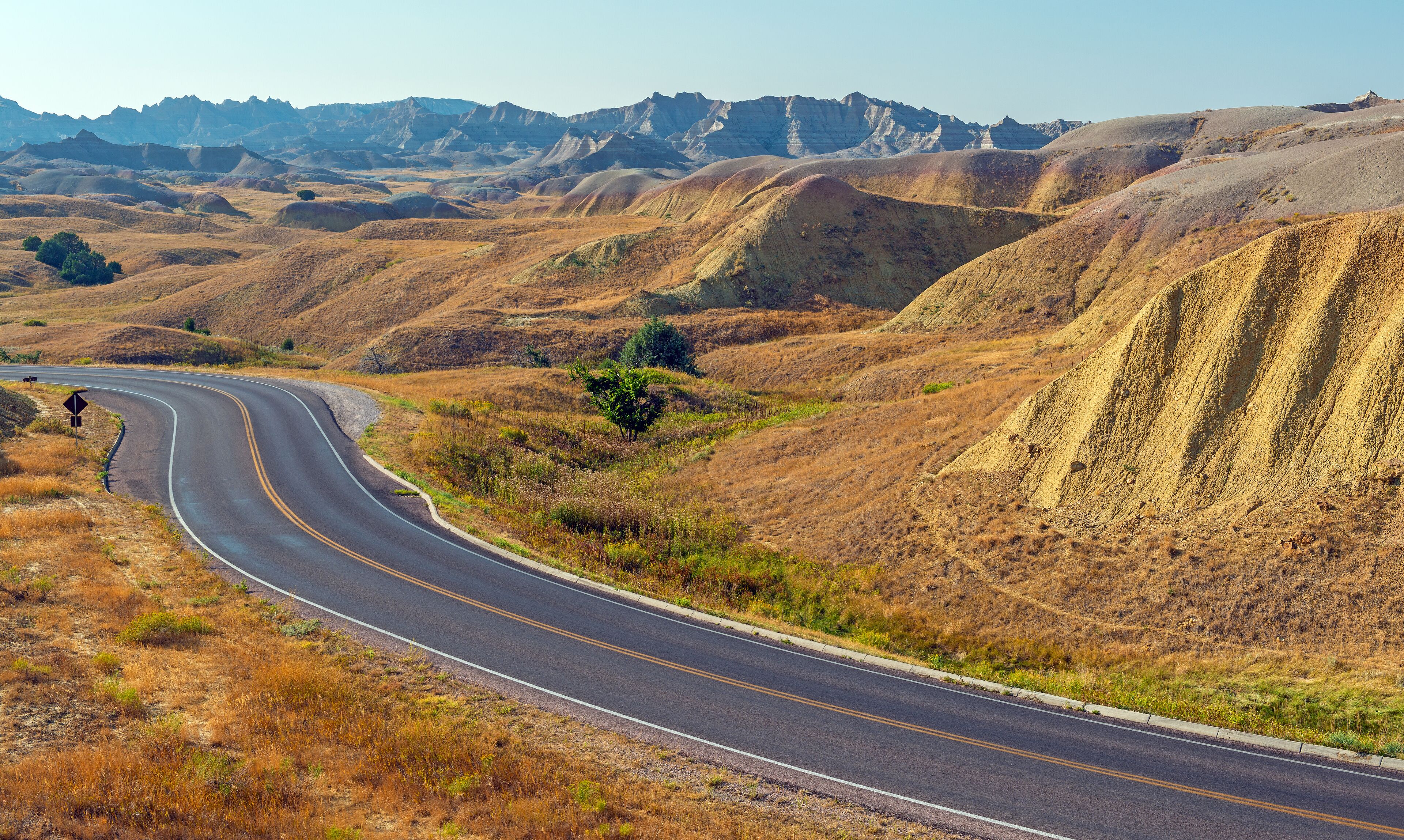 A winding road through a hilly landscape with sparse vegetation and distant mountains.