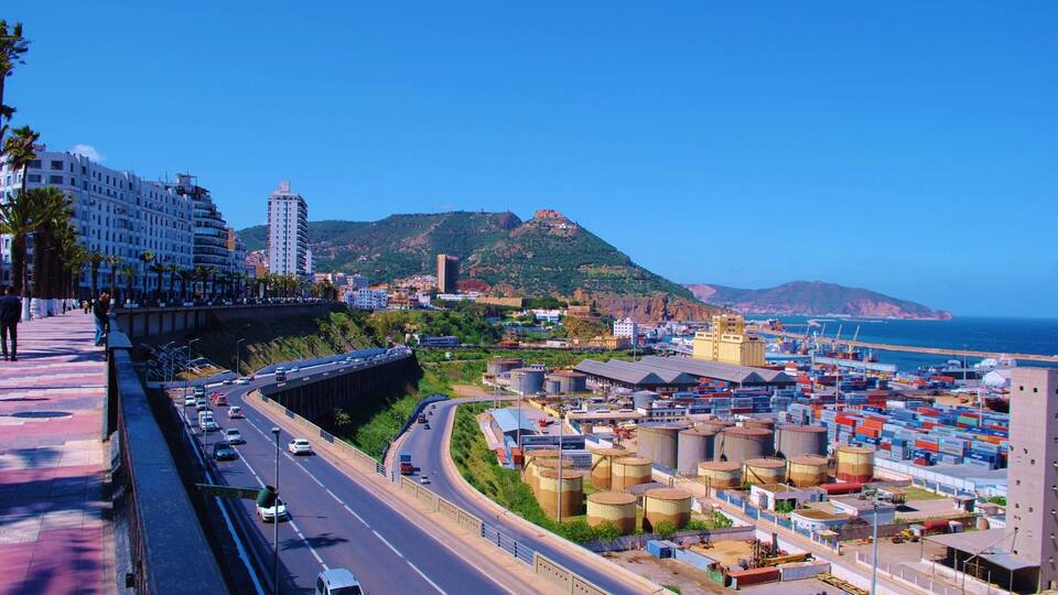 A coastal city with a highway, industrial area, and a mountain in the background.