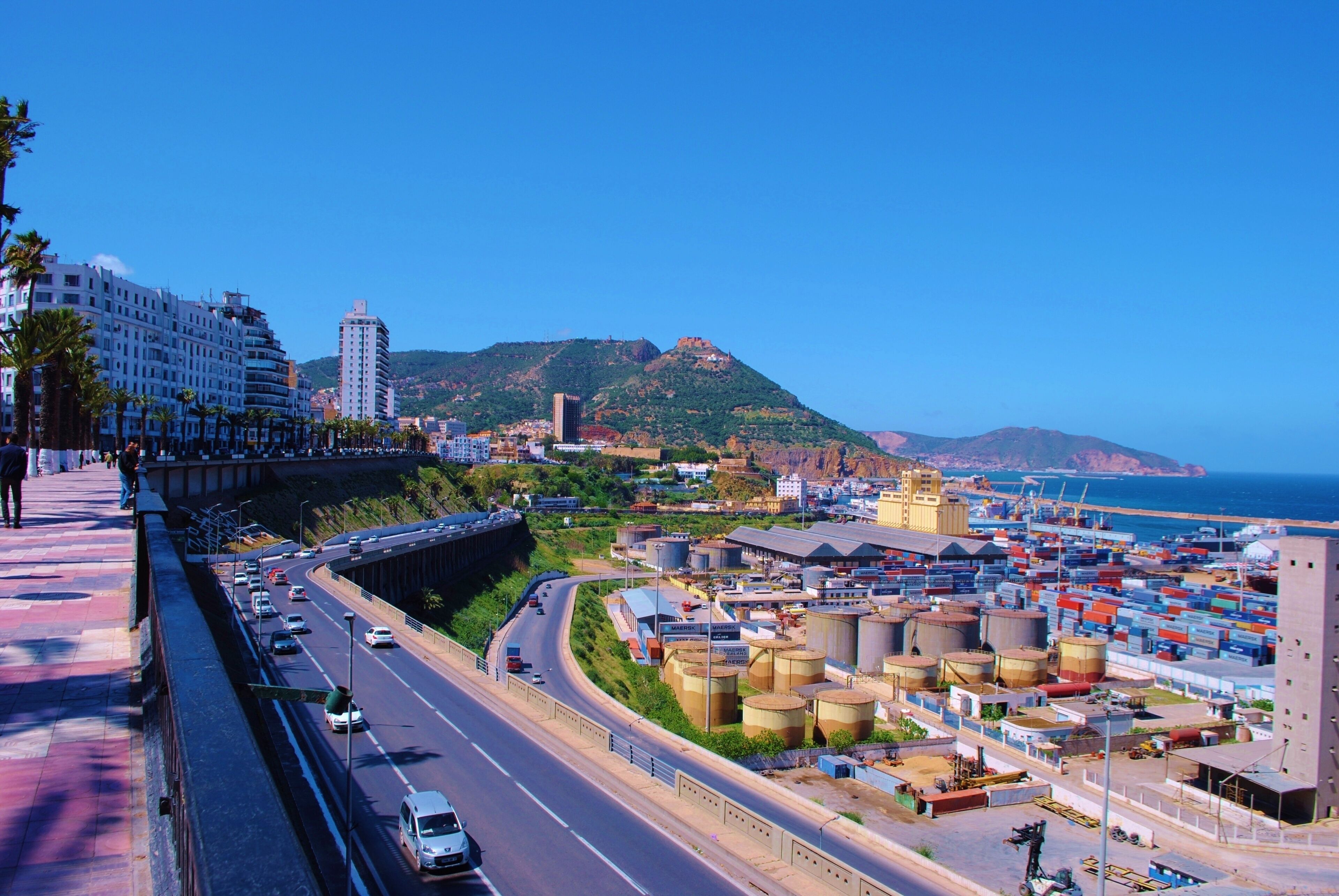 A coastal city with a highway, industrial area, and a mountain in the background.