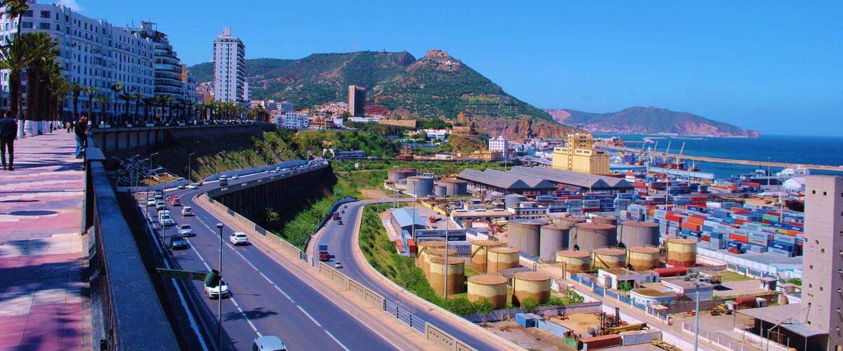 A coastal city with a highway, industrial area, and a mountain in the background.