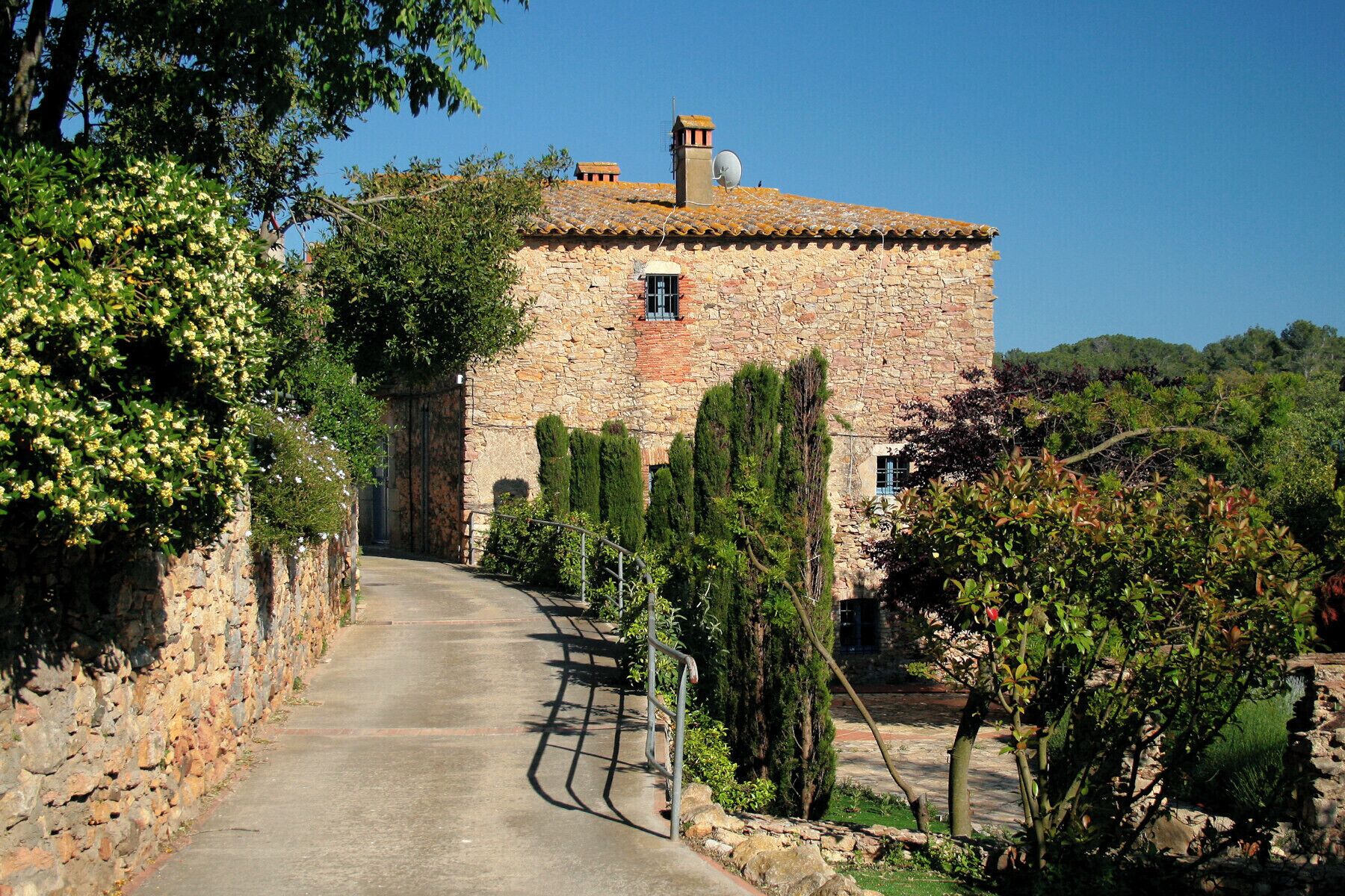 A stone building with a tiled roof, surrounded by greenery and a stone pathway.