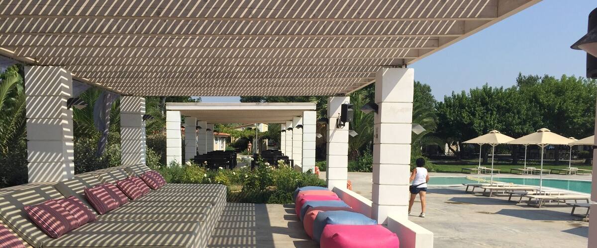 A covered outdoor seating area with patterned cushions and a pool in the background.