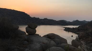 Un paisaje tranquilo junto al lago al atardecer, con grandes rocas y colinas al fondo.