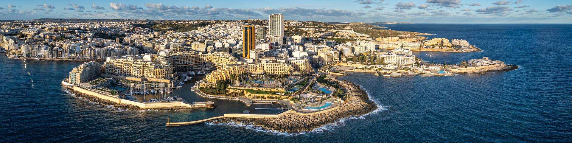 A coastal city with a marina, high-rise buildings, and a rocky peninsula.