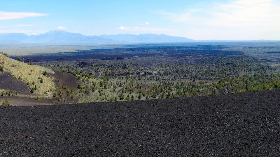 A volcanic landscape with a prominent hill, sparse vegetation, and distant mountains under a clear sky.