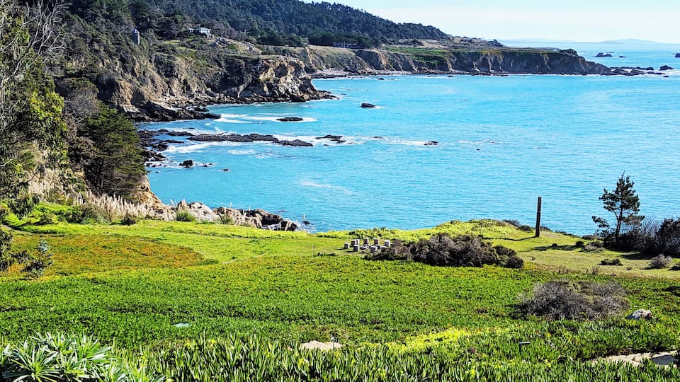 A coastal landscape with green fields, rocky cliffs, and a clear blue sea.