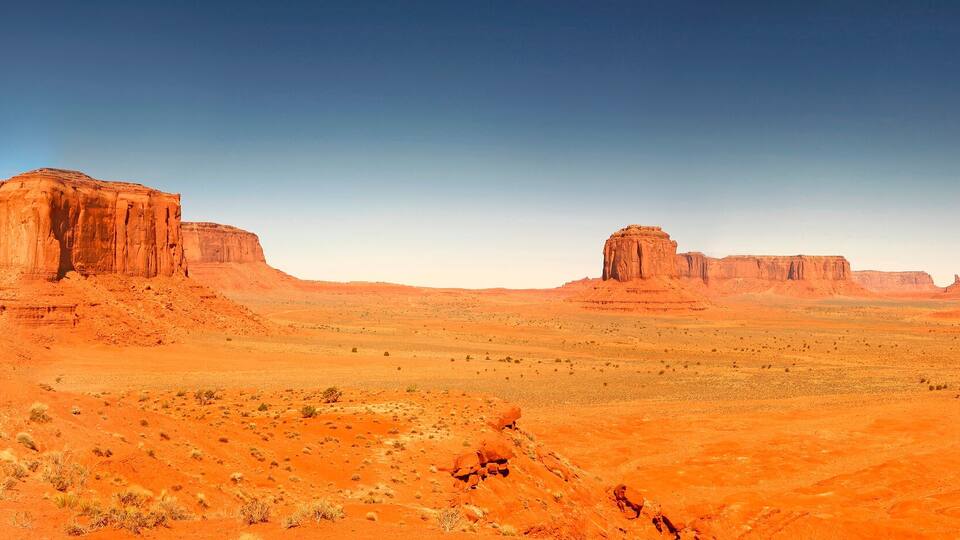 A desert landscape with prominent red rock formations and sparse vegetation.