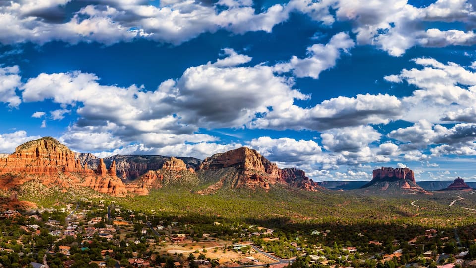 A desert landscape with red rock formations and a town in the foreground.