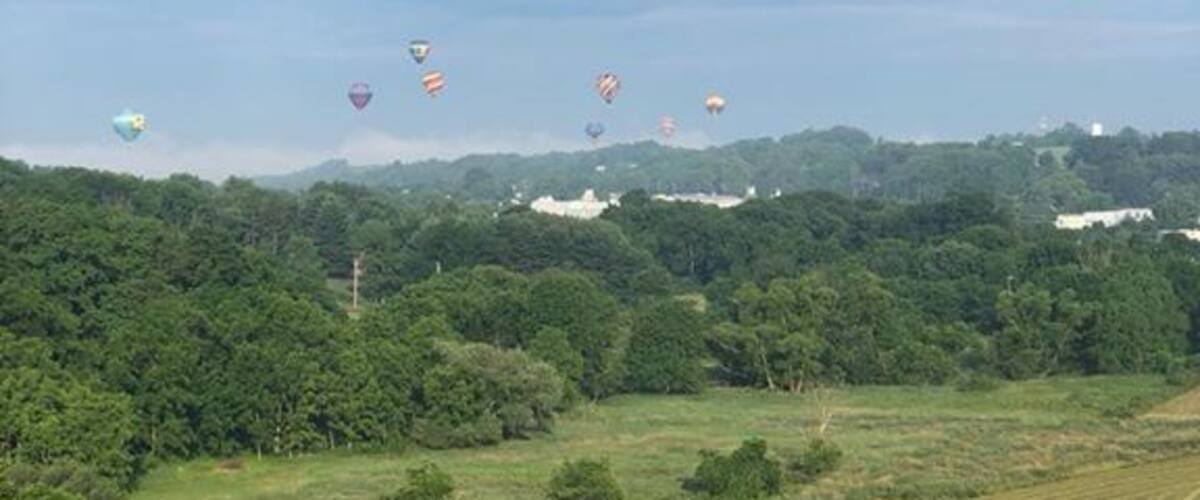 A landscape with a field of crops and several hot air balloons in the sky.