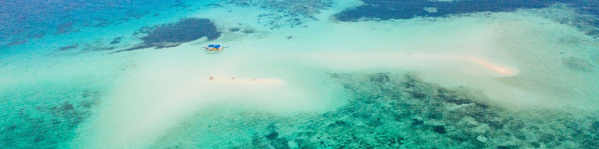 An aerial view of a turquoise sea with a small island and clear shallow waters.