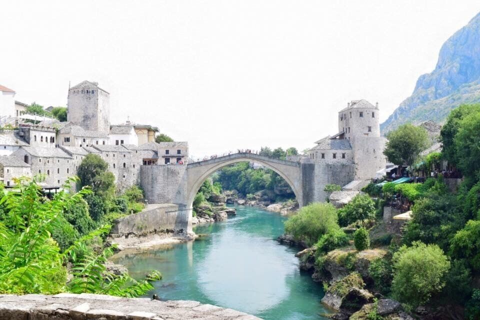 A stone bridge over a river, surrounded by historic buildings and lush greenery.