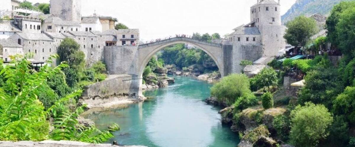 A stone bridge over a river, surrounded by historic buildings and lush greenery.