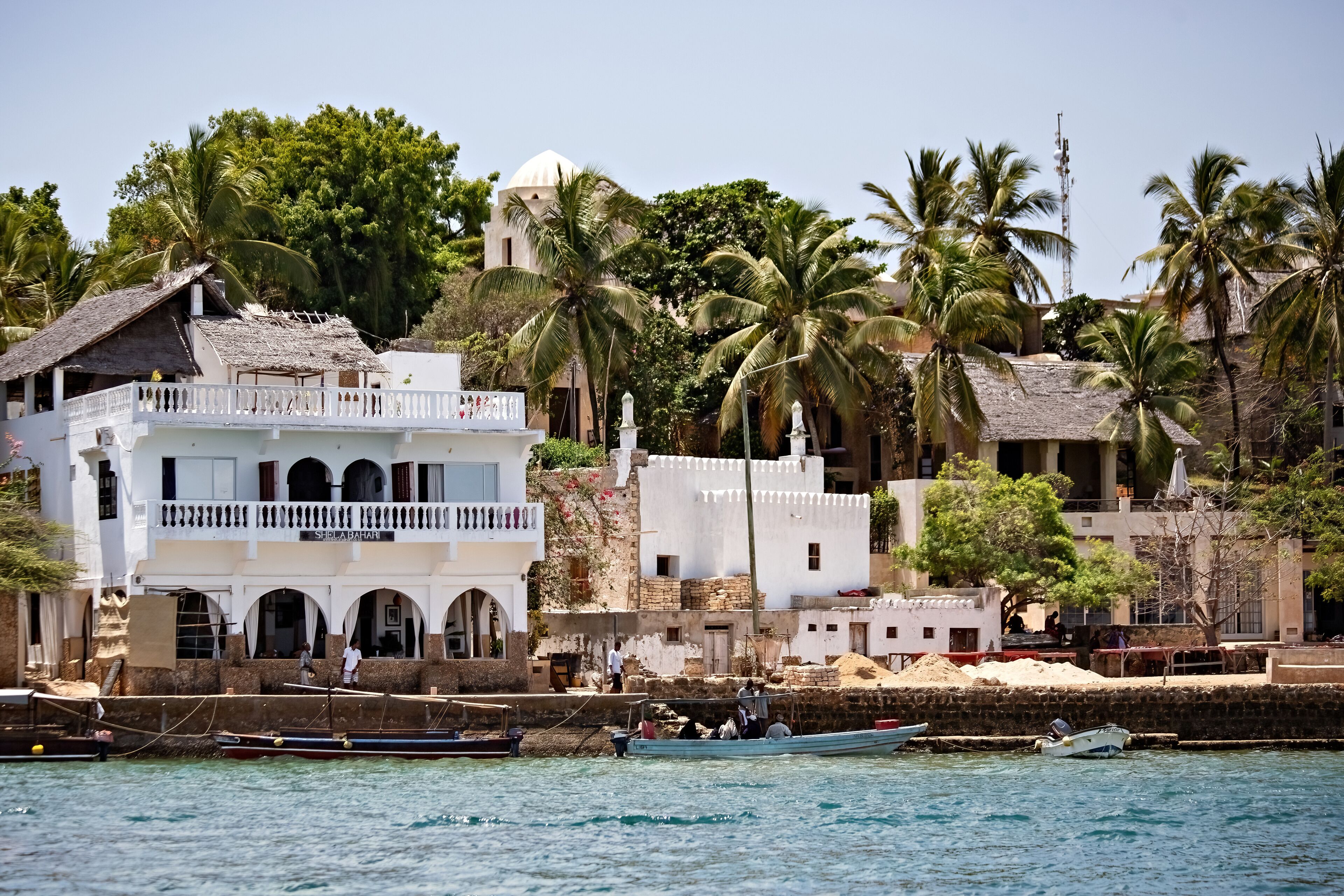 A coastal town with white buildings, palm trees, and boats on the water.