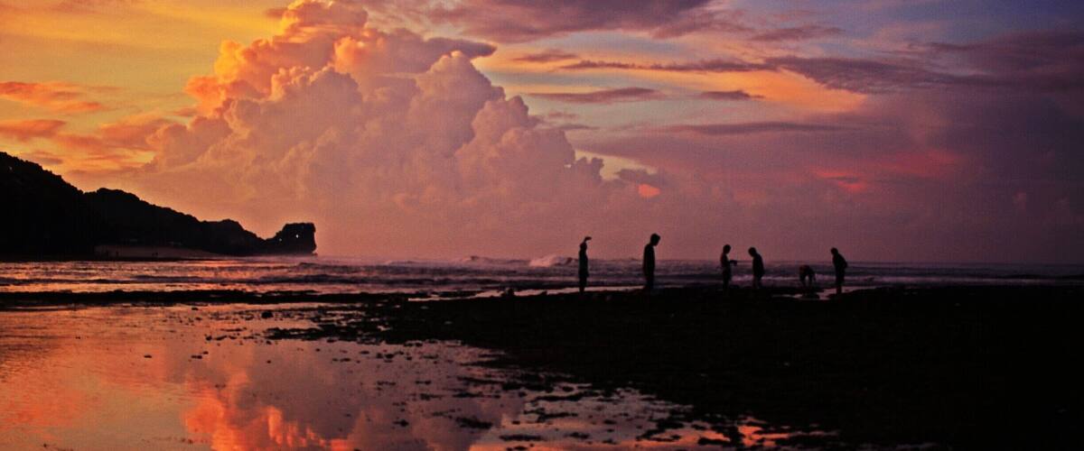A sunset over a beach with people standing on the shore.