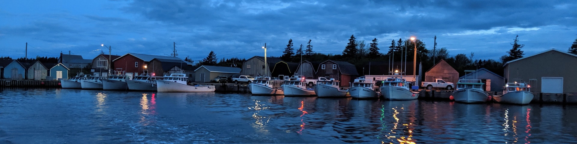 A harbor at dusk with boats docked, buildings, and a cloudy sky.