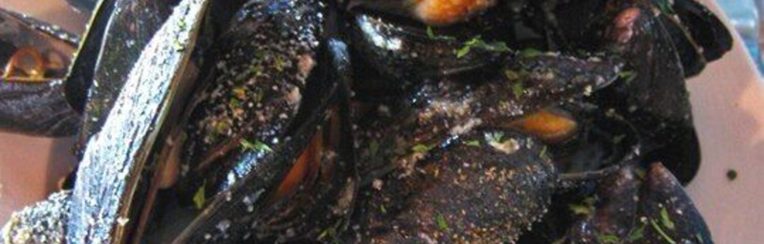 Un plato de mejillones cocinados con salsa para mojar.