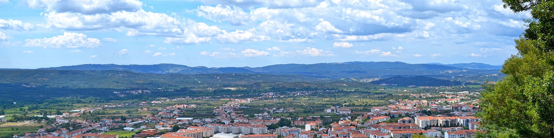 Vista panorámica de un pueblo con edificios de tejados rojos, rodeado de vegetación y colinas al fondo.