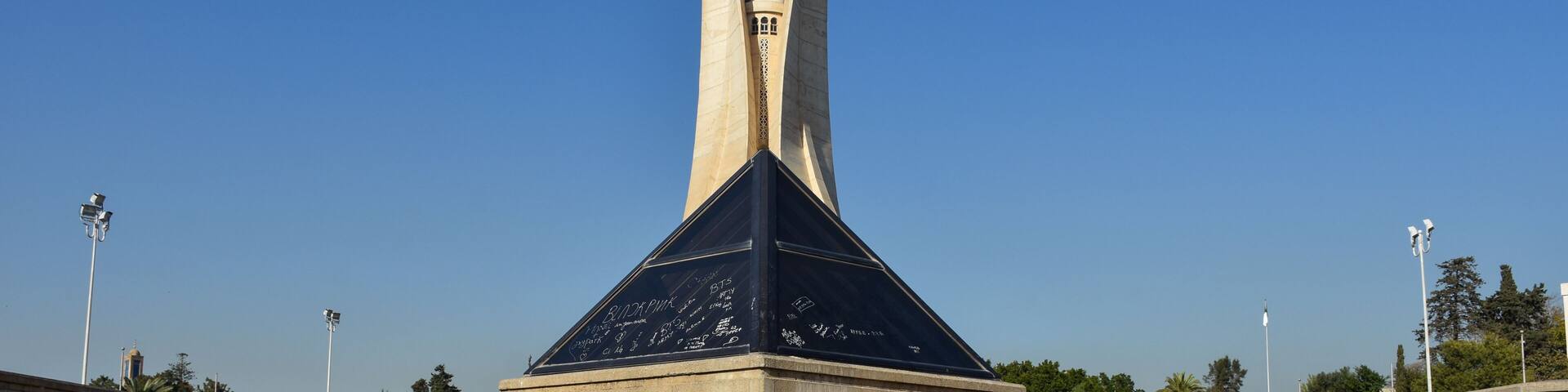 A pyramid-shaped monument with inscriptions, surrounded by a paved area and a clear sky.